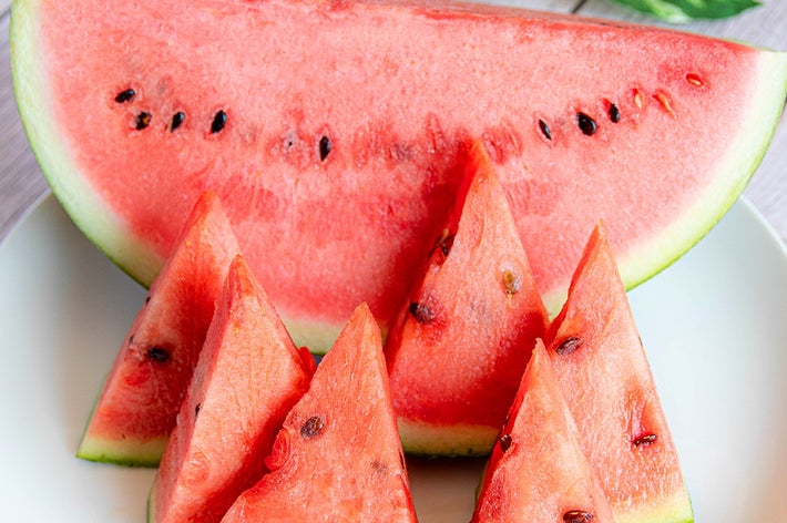 白い皿に盛られた切り分けられたスイカのスライス。背景に観葉植物の葉が見える。