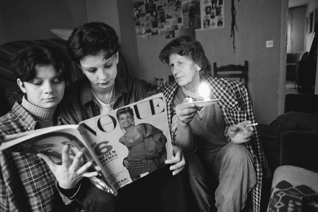 Three people sit closely, intently reading a Vogue magazine while one holds a candle
