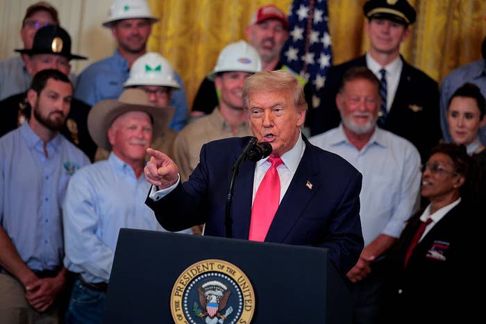 A idiosyncratic   speaks astatine  a podium with a statesmanlike  seal, surrounded by assorted  individuals successful  uniforms and enactment    attire