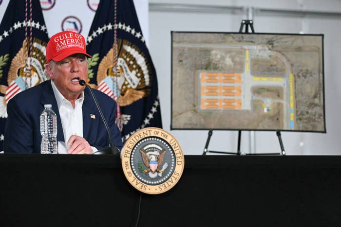 A antheral successful a Gulf of America chapeau speaks astatine a podium with a representation beside him and 2 U.S. seals successful the background