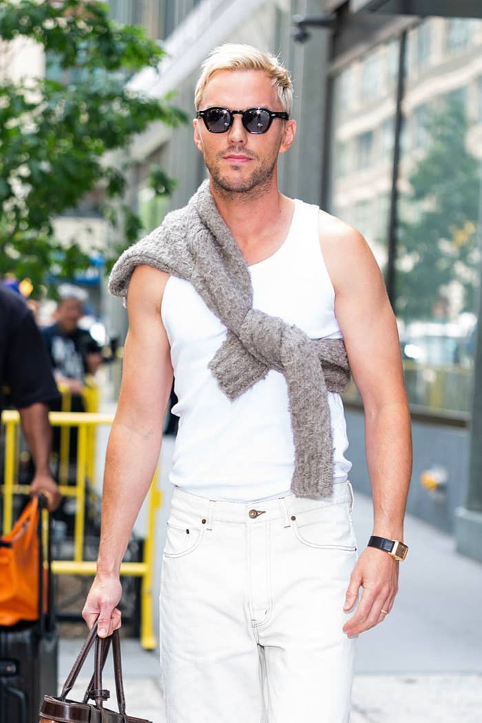 Man with sunglasses successful  a achromatic  vessel  apical  and jeans, sweater draped implicit    shoulders, walks connected  a metropolis  thoroughfare  holding a bag
