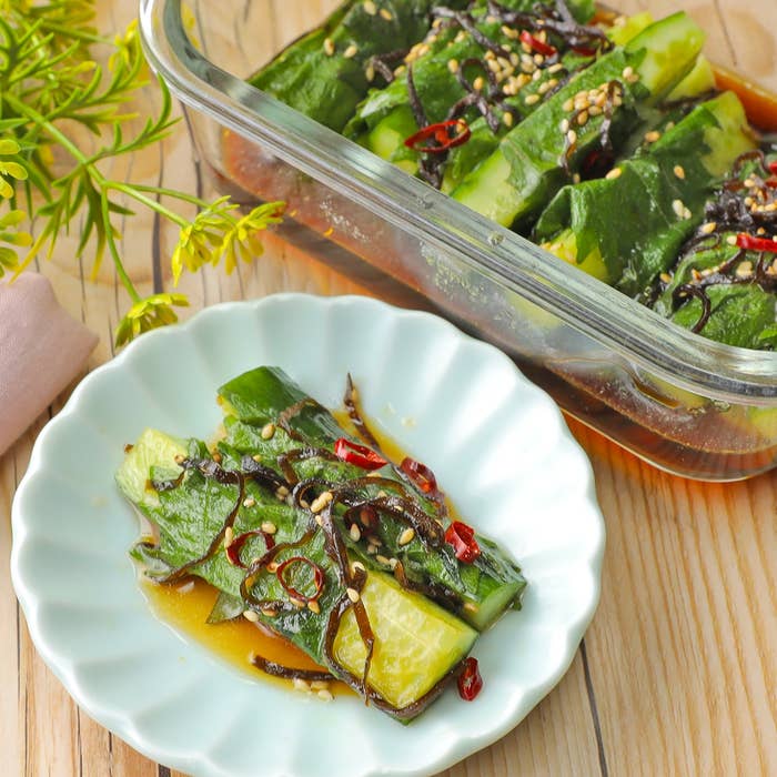 お皿に盛られた調味料を添えたきゅうりと昆布の漬物。隣に同様の料理が入ったガラス容器。