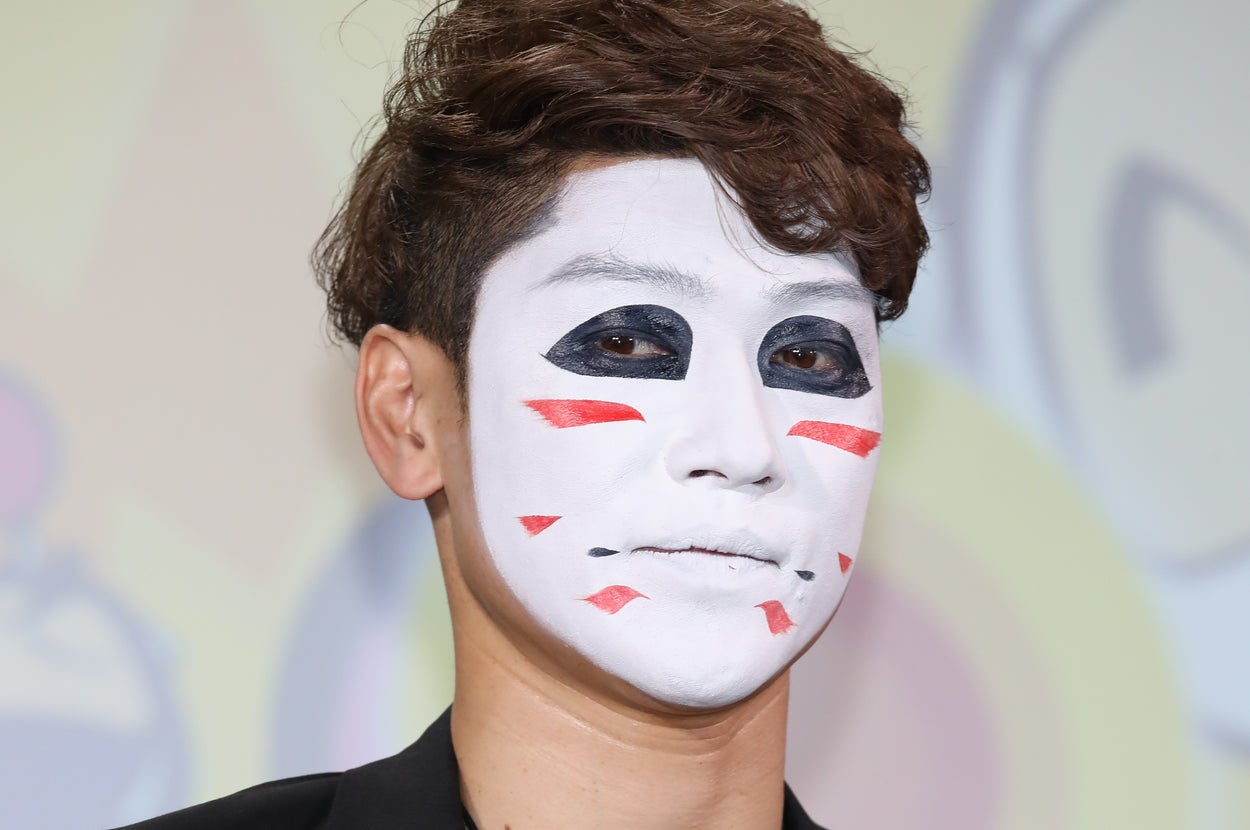 白いフェイスペイントを施し、黒のジャケットとビーズのネックレスを身に着けた男性。
