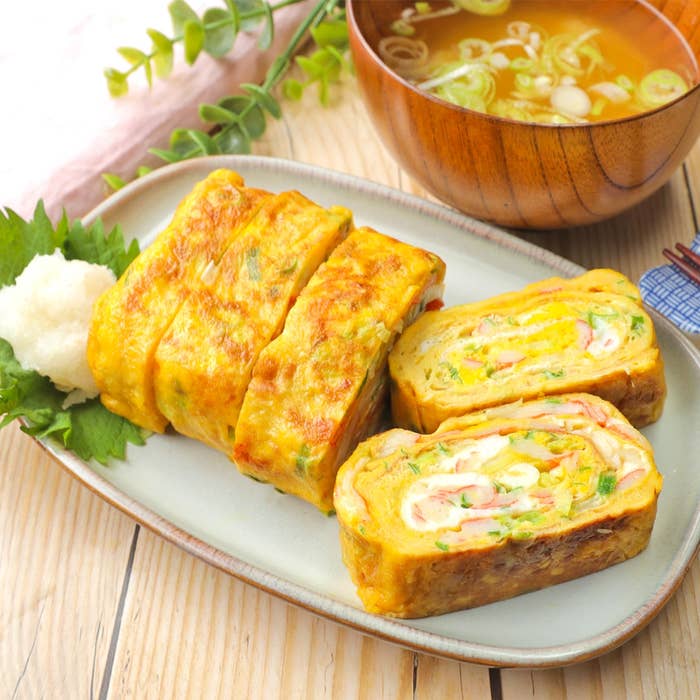 卵焼きと味噌汁のセット。卵焼きにはネギとハムが巻き込まれている。木のテーブルに盛り付けられている。