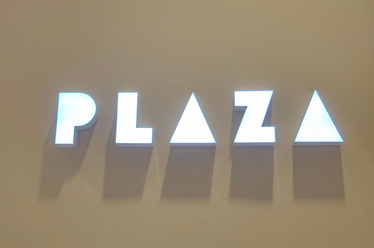 「PLAZA」と光る文字の壁看板。