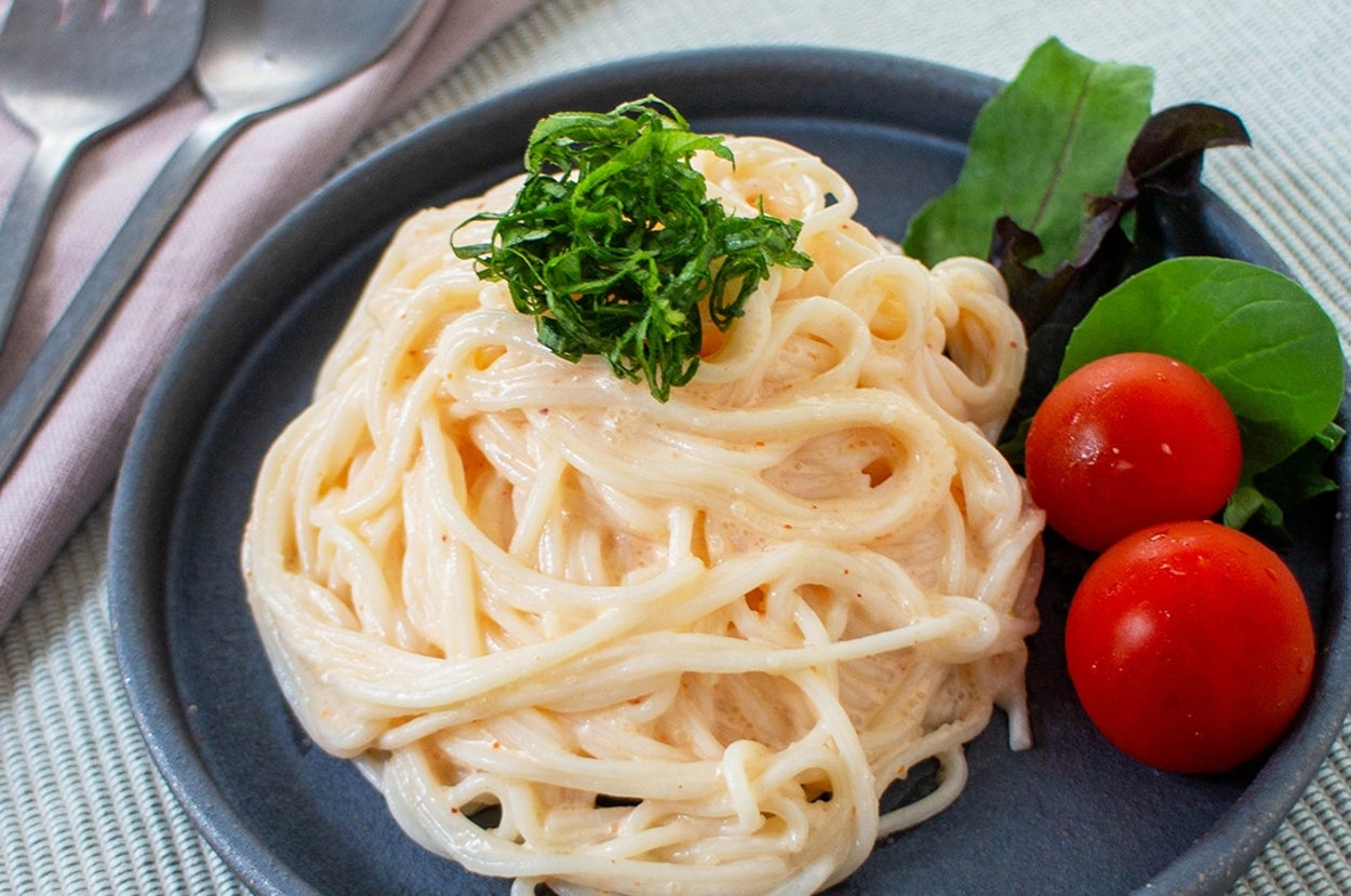 お皿に盛られたクリーミーなパスタ。上に緑のトッピング、サイドにミニトマトと葉野菜が添えられている。