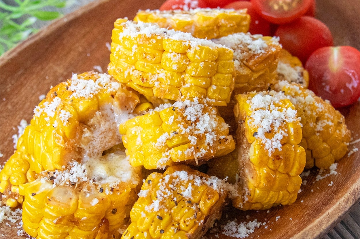 木製皿に盛られたとうもろこしのガーリックバター焼き。粉チーズとコショウがかかっている。