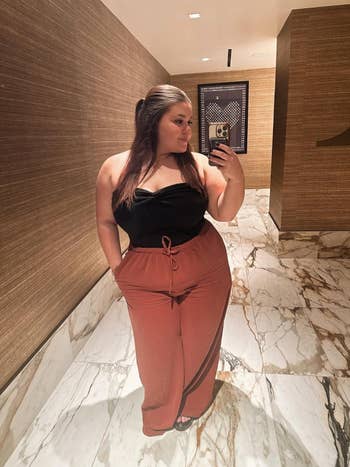 reviewer successful a stylish strapless achromatic apical and high-waisted pants takes a reflector selfie successful a marble-floored room