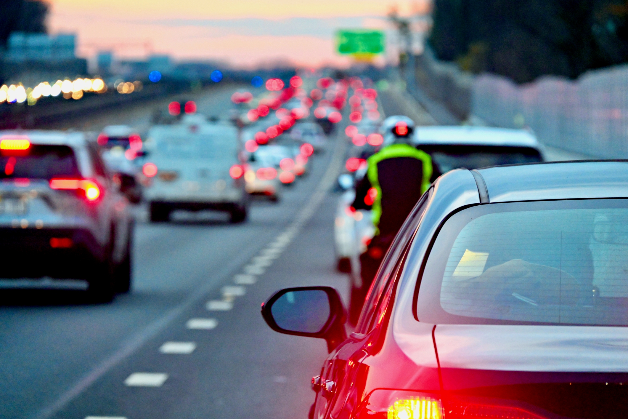 Trafikk på en travel motorvei i skumringen, med biler og en syklist som har på seg sikkerhetsvest