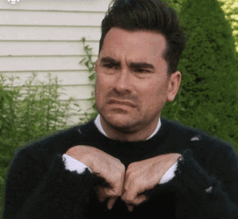 Person with skeptical expression, hands in front, miming claws. Background includes greenery and a house. #SchittsCreek displayed at top