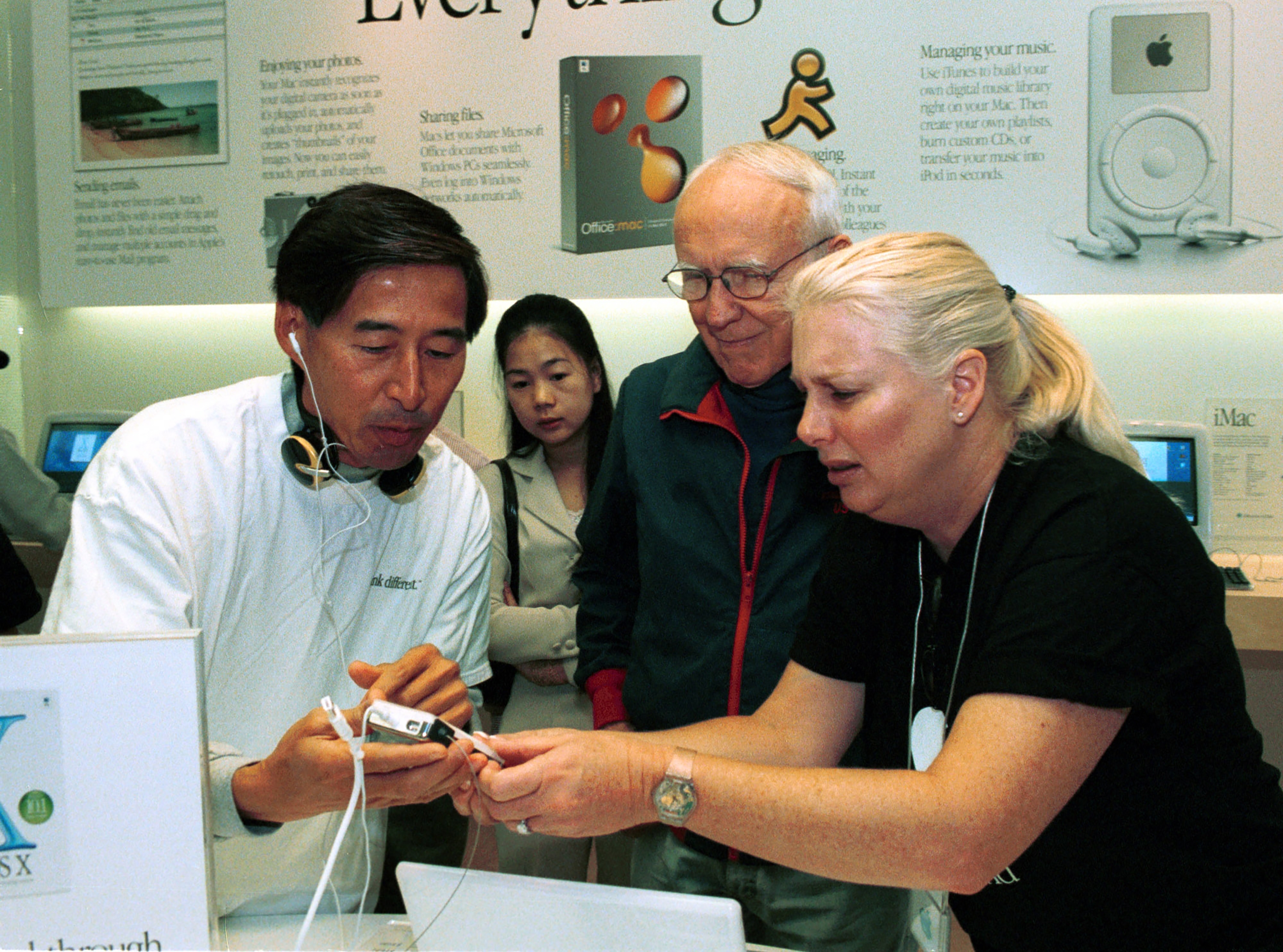 Two Apple Store employees assist an older customer with an iPod device in a store setting