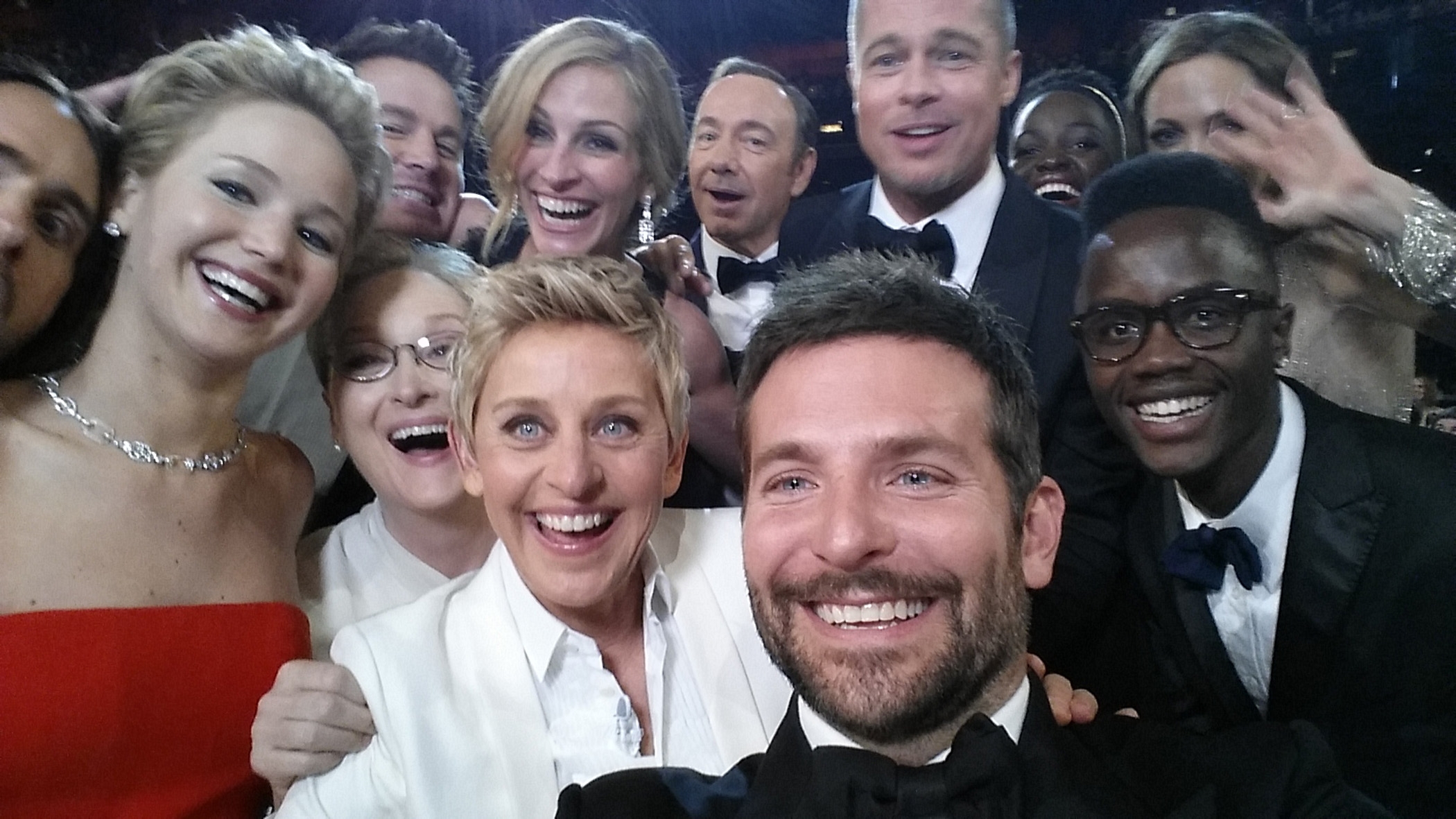 Group of celebrities posing for a selfie at an event, smiling and cheerful, wearing formal attire including tuxedos and gowns