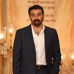 A man in a sharp suit poses confidently at a formal event, with an elegant backdrop and ornate lighting
