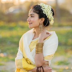 Person wearing traditional attire with intricate jewelry and floral hair adornment, looking to the side in an outdoor setting