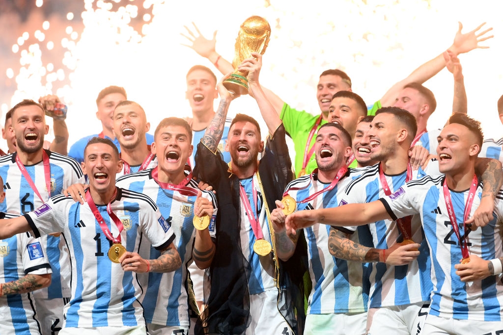 Soccer team celebrates with gold medals and a trophy, cheering energetically on a victory stage