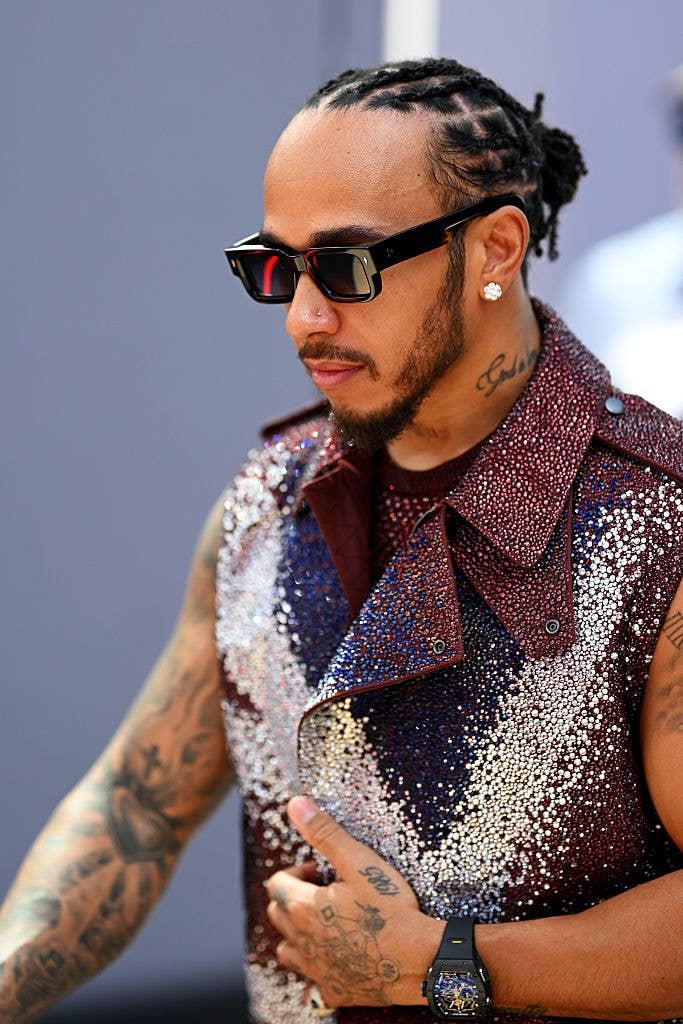 A person with tattoos wearing sunglasses and a sparkling, sleeveless sequined vest