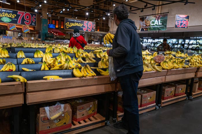 Person buying for bananas successful a market store, surrounded by ample displays of effect with varying prices