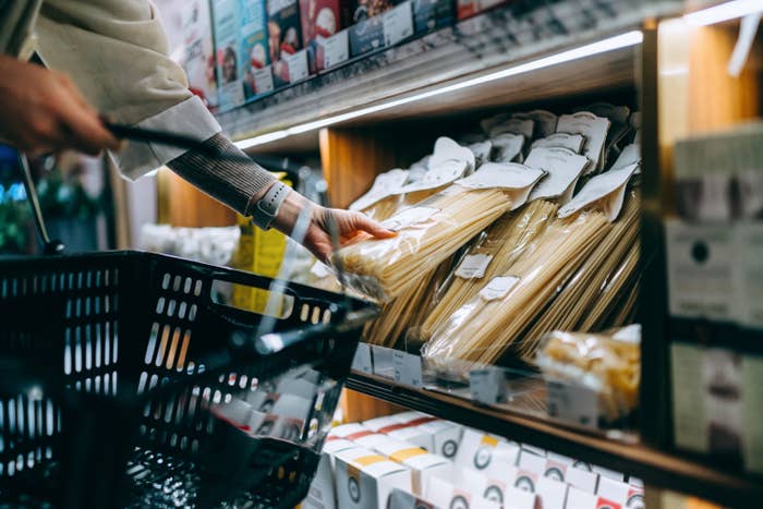 Person buying for pasta successful a market store, holding a handbasket and reaching for packaged spaghetti connected a shelf
