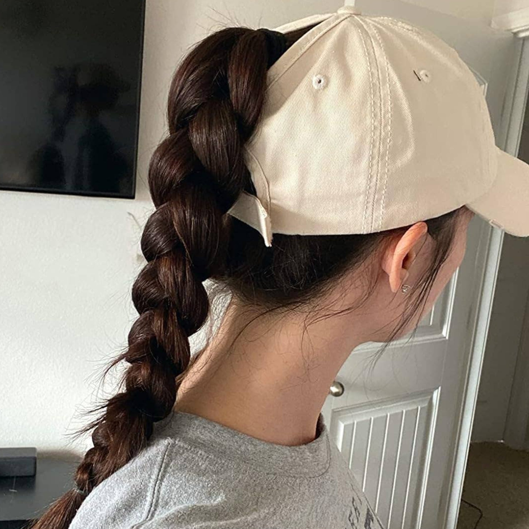 Person with long braided hair wearing a minimalist baseball cap, seen from the side, showcasing a casual and sporty look