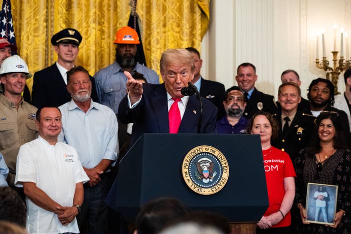 Donald Trump speaking astatine a podium with statesmanlike seal, surrounded by people, including workers and uniformed personnel, successful a ceremonial setting