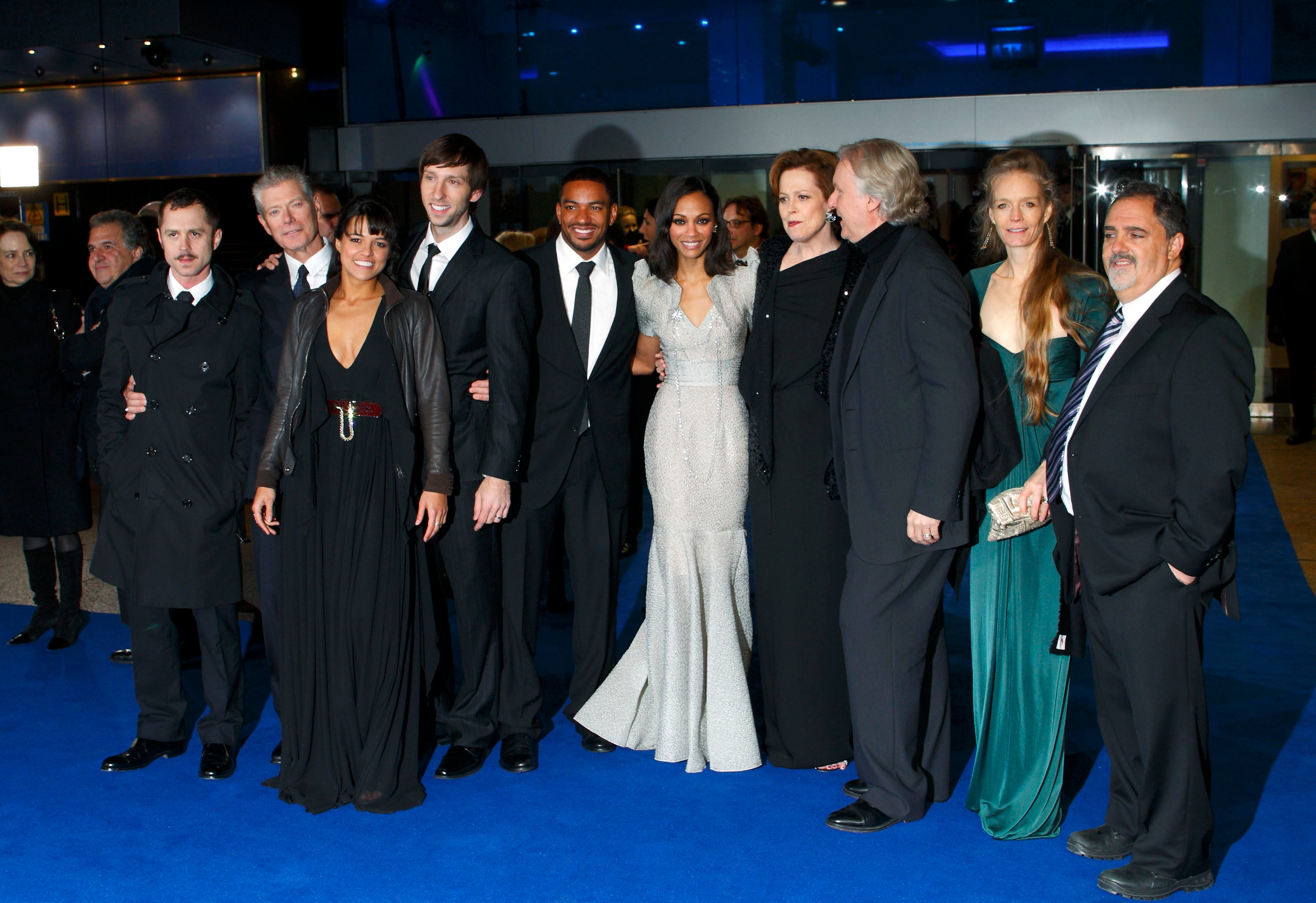 A group of people in formal attire pose together on a blue carpet at an event