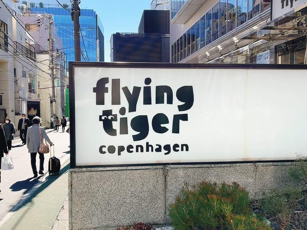歩道沿いにフライングタイガーコペンハーゲンの看板がある都市の風景。人々が歩いています。