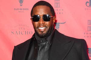 Man on red carpet wearing a sleek leather outfit and sunglasses, with a tailored jacket, posing confidently against a branded backdrop