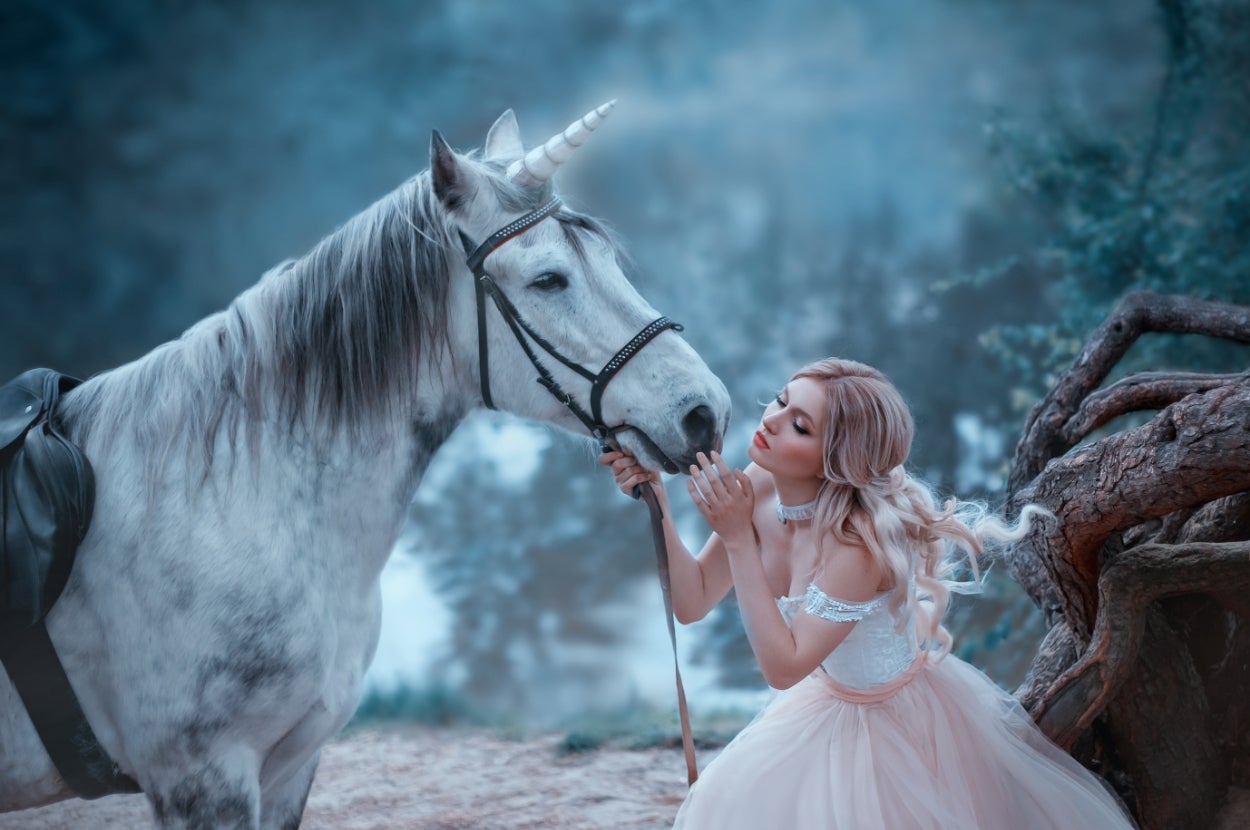 Woman in an enchanting gown gently caresses a unicorn in a mystical forest setting