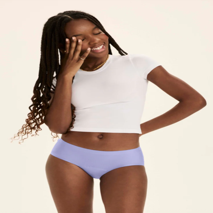 Person in a white cropped shirt and underwear poses with a hand on cheek, smiling, as part of a shopping feature