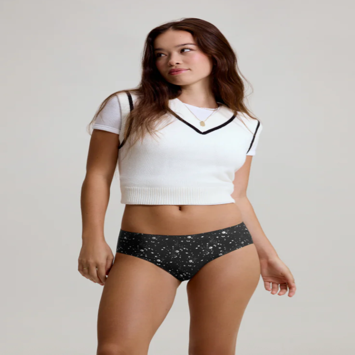 Woman modeling a white cropped V-neck sweater and star-patterned underwear in a studio setting