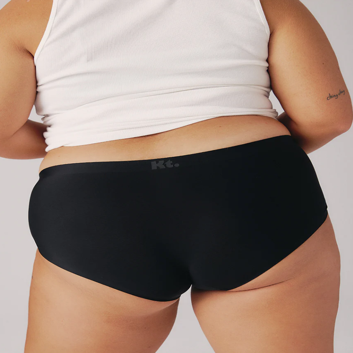 Person wearing a white tank top and black underwear, shown from the back, highlighting comfortable, everyday wear