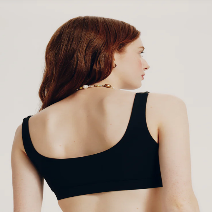 Person with long hair models a minimalist, sleeveless top, showcasing its back design, suitable for shopping or fashion-focused content