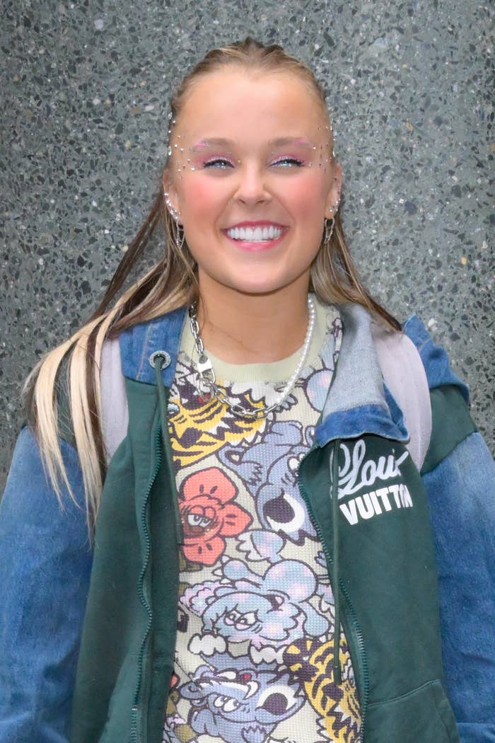 Smiling idiosyncratic   with embellished makeup, wearing a floral sweater nether  a Louis Vuitton jacket, lasting  against a speckled chromatic  background