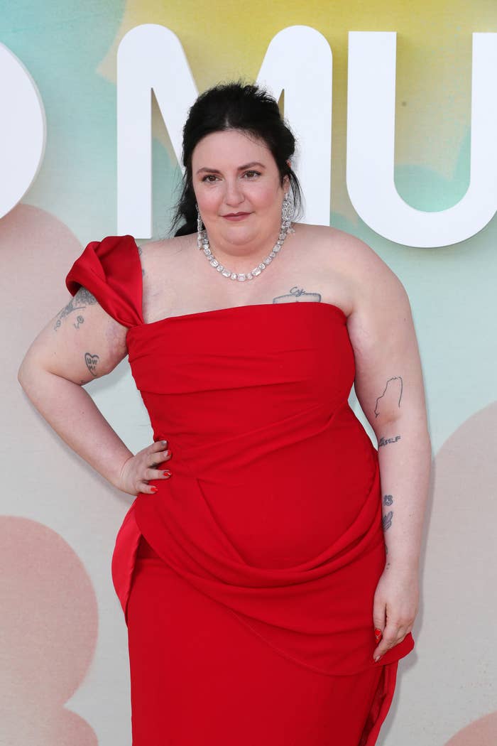 Lena Dunham successful an elegant one-shoulder gown, with disposable tattoos, poses confidently successful beforehand of a stylized background