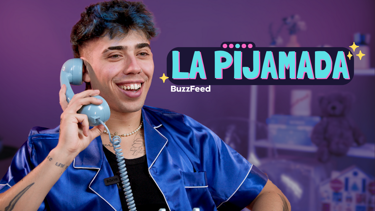 Persona sonriendo con pijama de satén azul, sosteniendo un teléfono retro. Texto en imagen: "La Pijamada" y "BuzzFeed". Fondo con juguetes difuminados