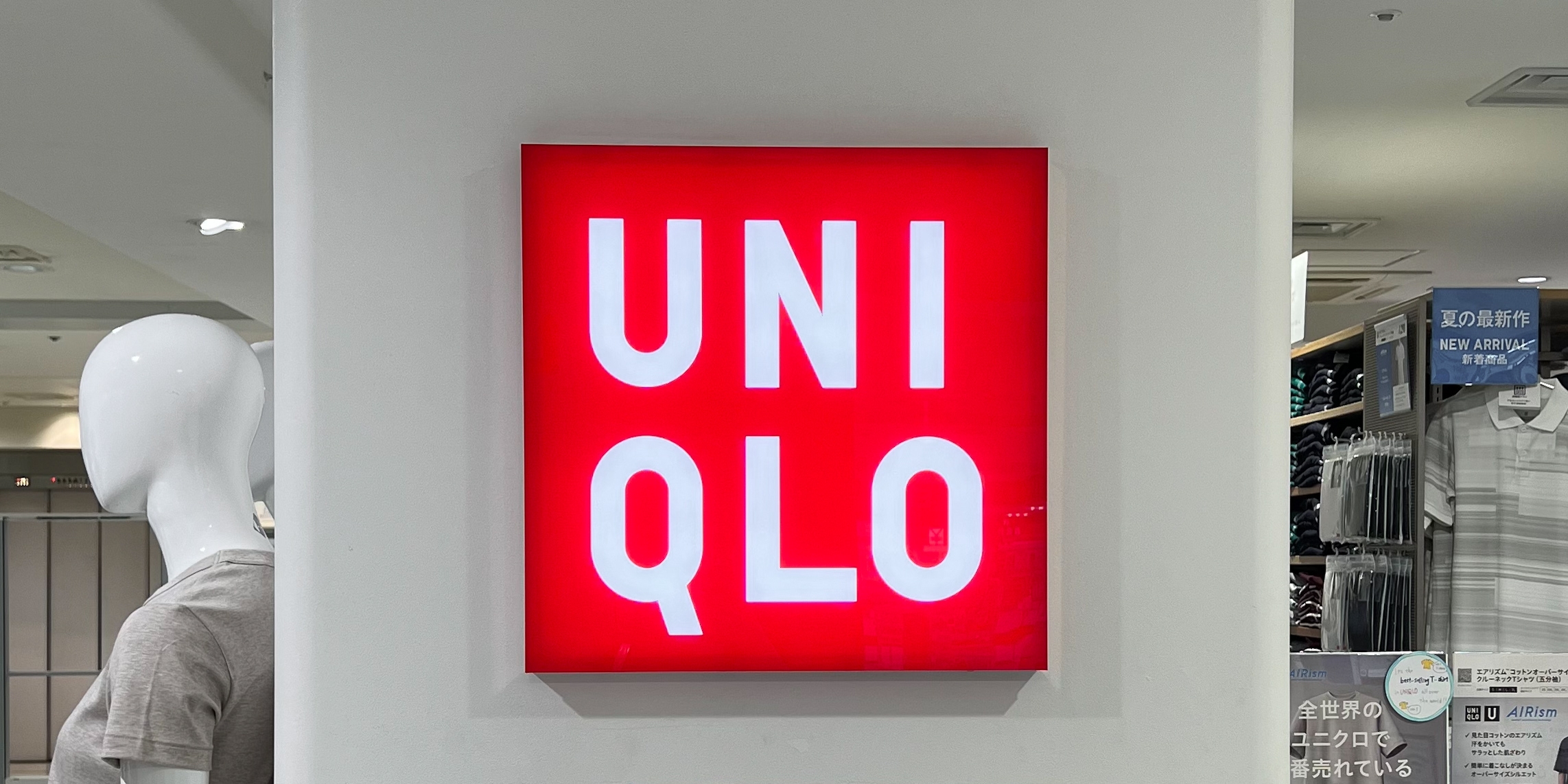 Uniqlo store sign with bold white letters on a red background. Mannequin visible on the left side