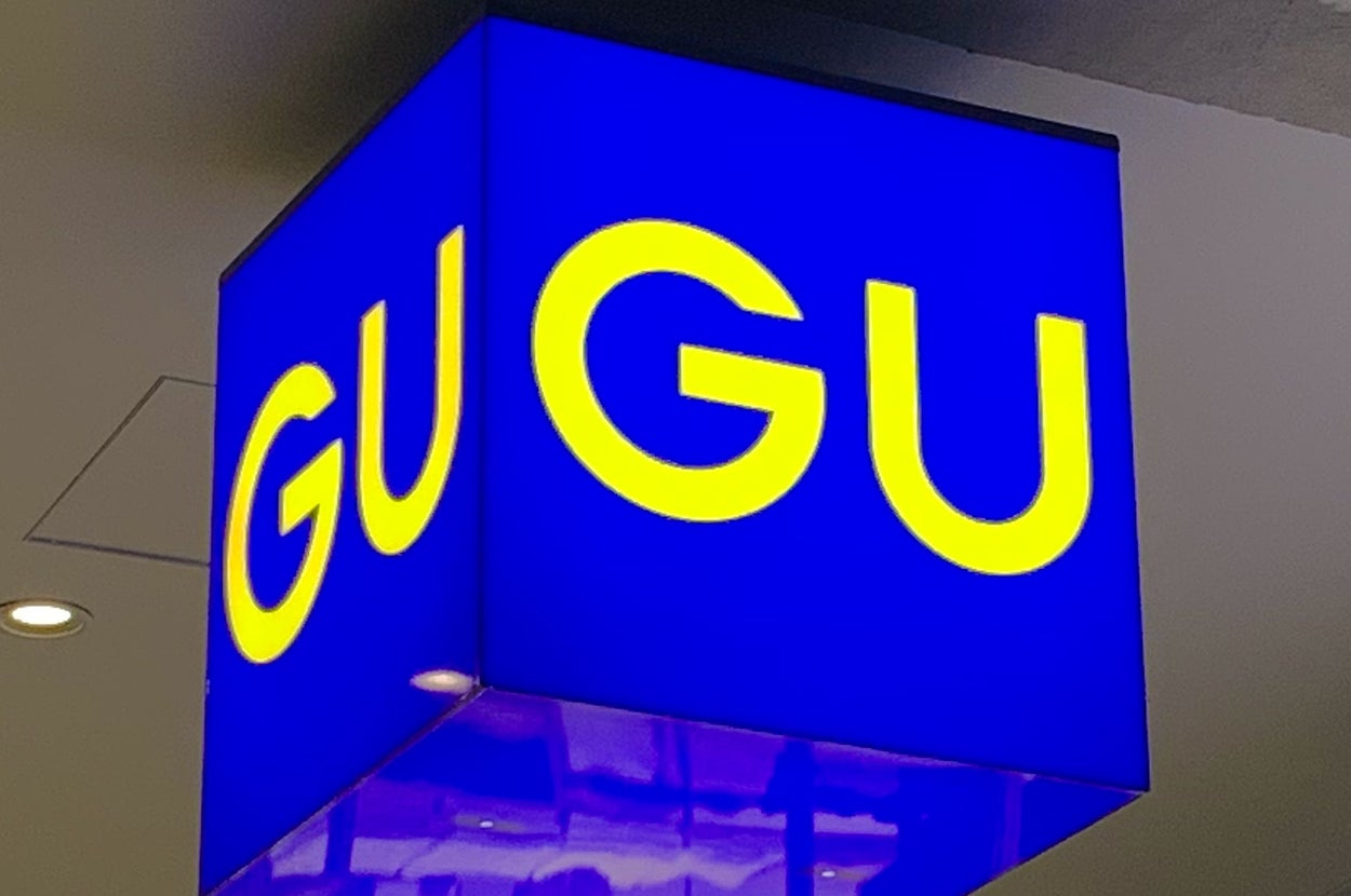 Overhead view of a cube-shaped blue sign with yellow "GU" letters, hanging in a well-lit indoor space