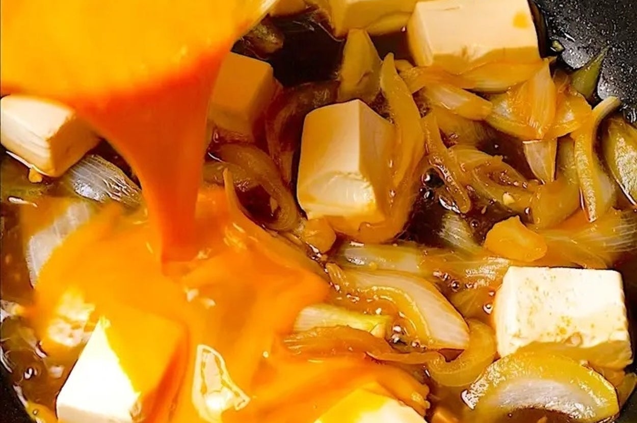 玉ねぎと豆腐が入ったフライパンに鮮やかな液体が注がれている。料理過程を示す。