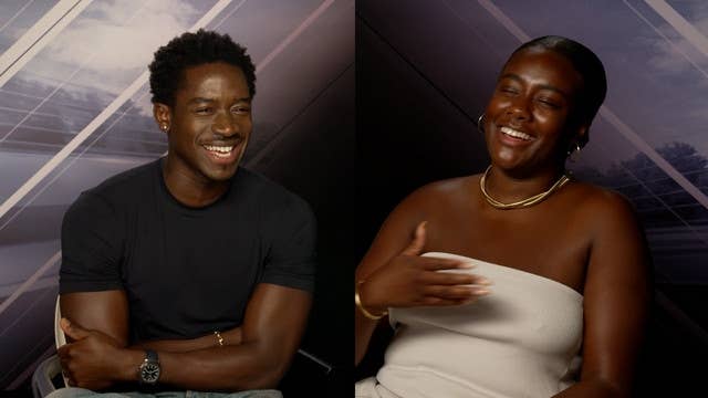 Two people seated, both smiling and laughing in an interview setting. The person on the left wears a casual t-shirt; the person on the right wears a stylish strapless top