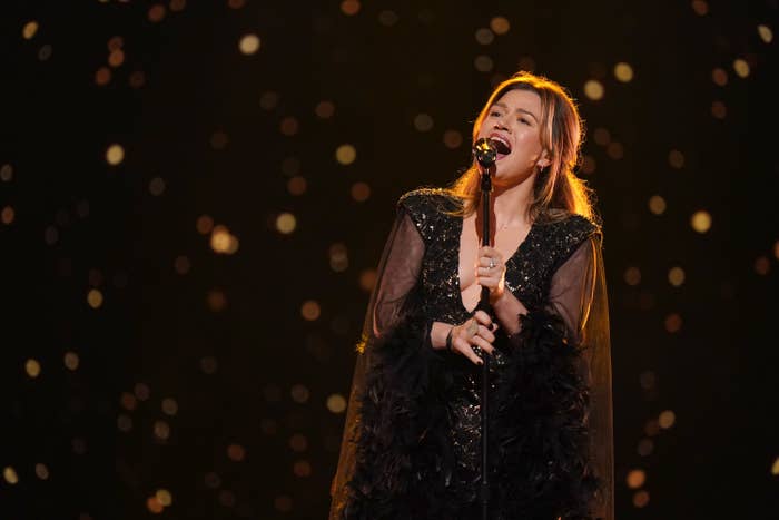 Singer performing passionately connected  stage, wearing a achromatic  outfit with feather details, successful  beforehand   of a sparkling background
