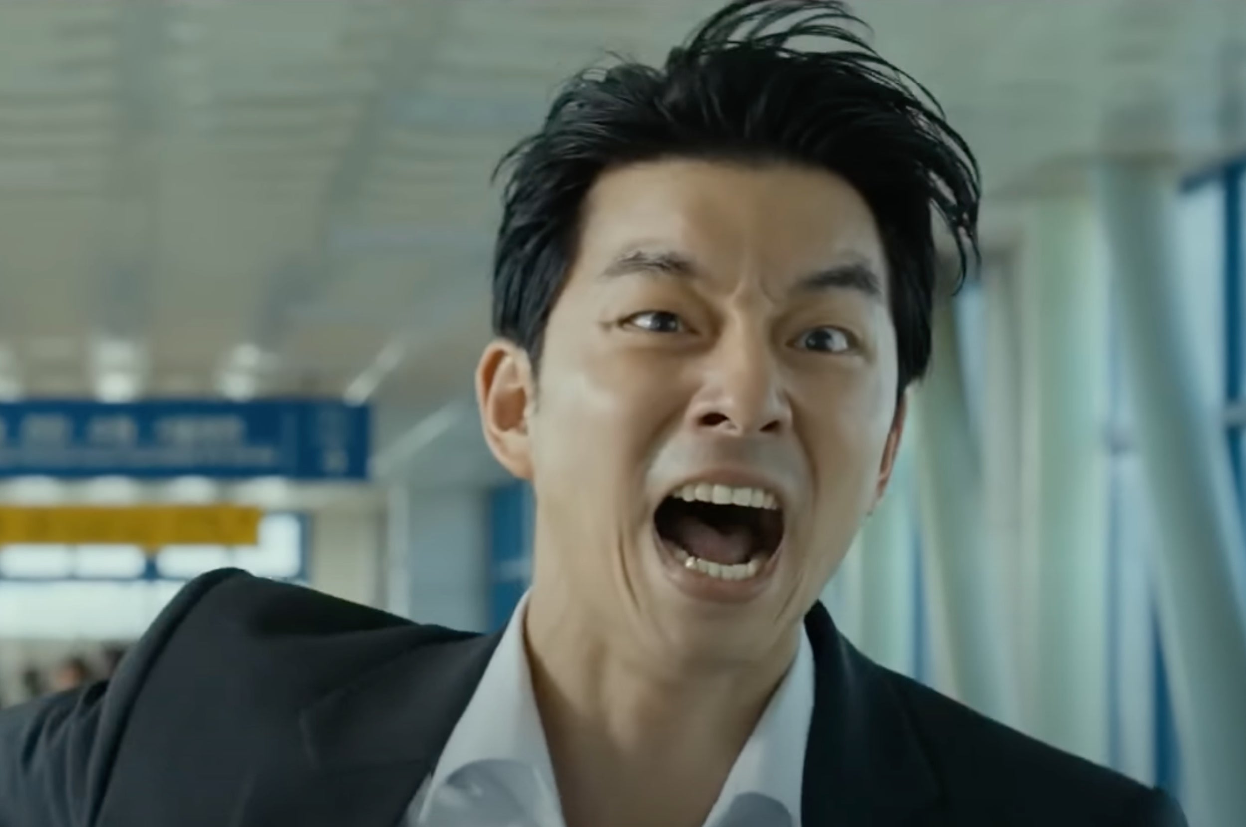 Person in a suit is yelling with an open mouth in an indoor setting, appearing intense and animated