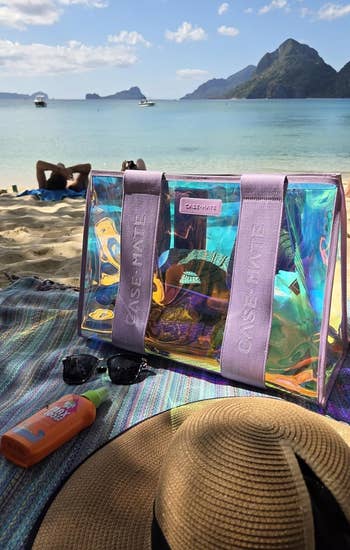 Beach country with a transparent Case-Mate tote, sunscreen, sunglasses, and a straw chapeau connected a colorful towel. Scenic presumption of oversea and mountains successful background