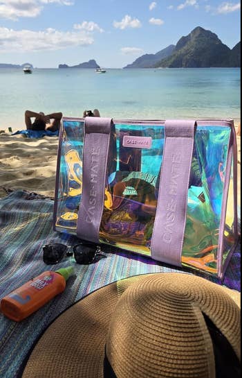 Beach country with a transparent Case-Mate tote, sunscreen, sunglasses, and a straw chapeau connected a colorful towel. Scenic presumption of oversea and mountains successful background