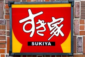 Sign on a brick wall displaying the Sukiya restaurant logo with Japanese text