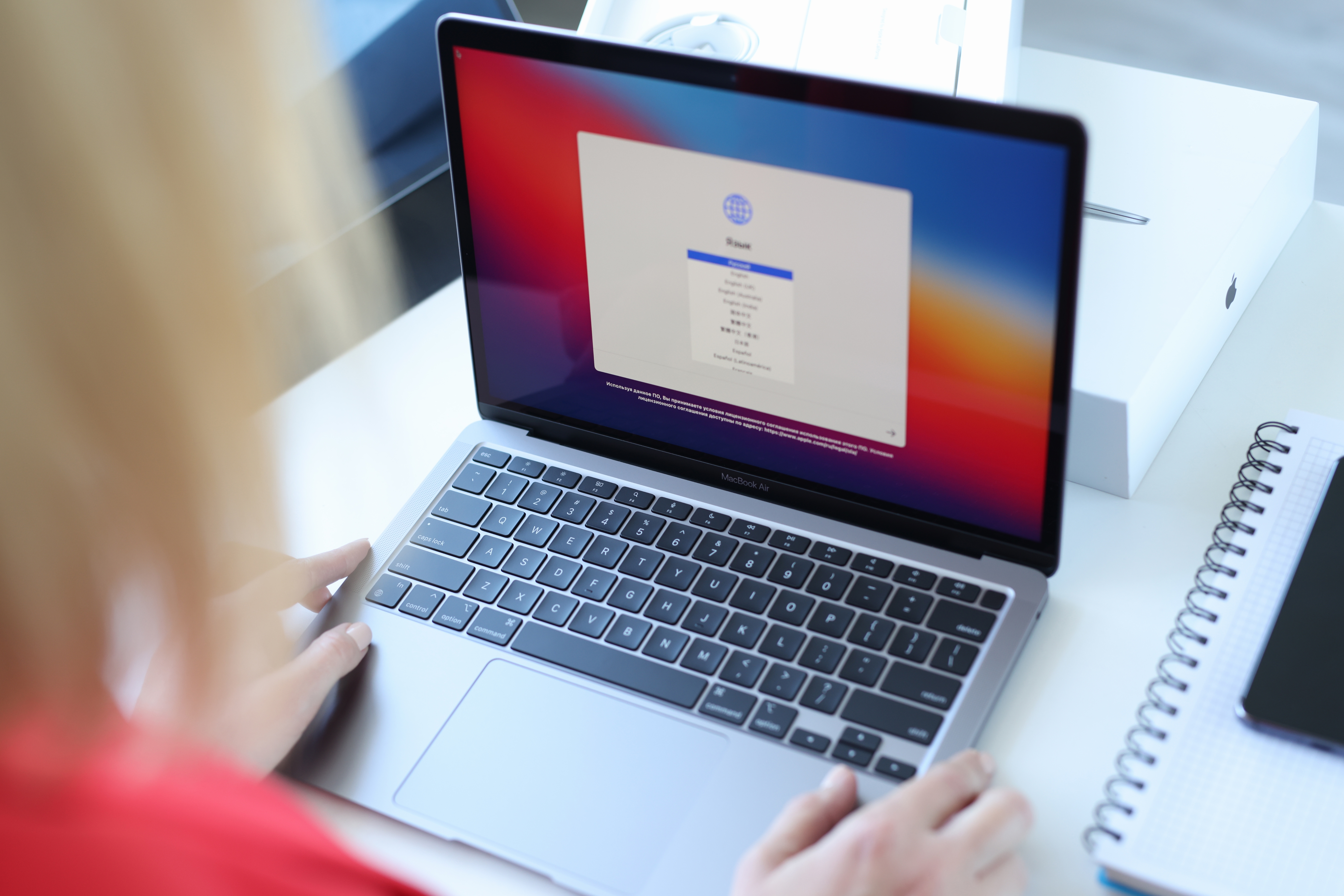 Person setting up a new laptop, navigating the setup screen. A notebook is nearby on the desk