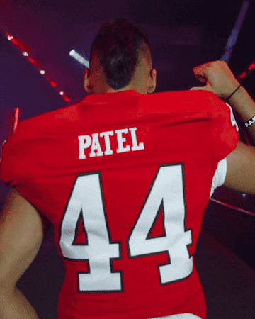 Football player in a red jersey with the name &quot;Patel&quot; and number 44 celebrates in a dimly lit area with flashing lights