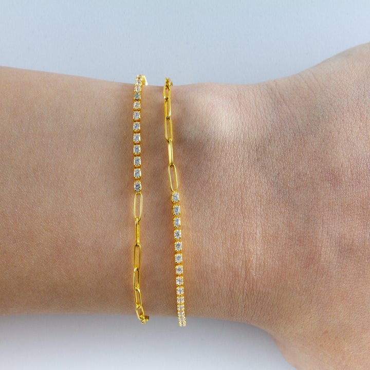 Two gold chain bracelets with sparkling stones on a person's wrist