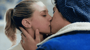 Two people share a close, intimate kiss. One wears a beanie, and their hands gently touch their faces