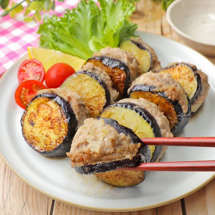 皿に盛られたナスと肉のはさみ焼き。トマトとレタスが添えられている。箸で一切れ持ち上げられている。