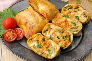 お皿に鶏肉と野菜やチーズが入ったカットロール、トマト、葉物とガラスの飲み物が置かれている食事風景。
